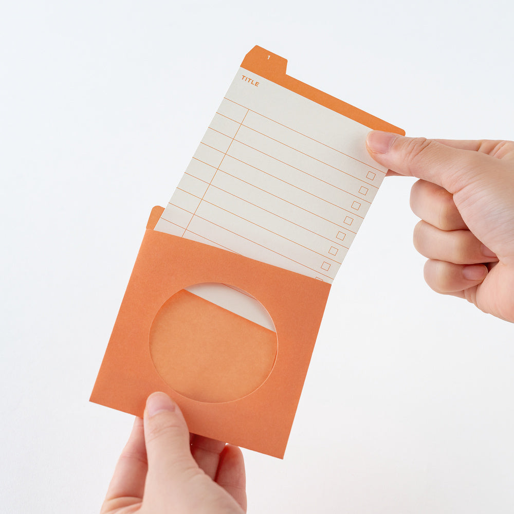 An orange pocket organizer with a circular cutout, holding an orange and white lined notepad, held by two hands against a white background.