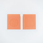 Two orange paper envelopes on a plain white background, one showing a circular cutout and the other plain.