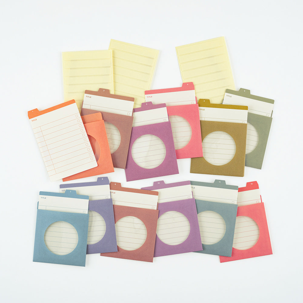 A set of colorful paper divider tabs and notepads arranged on a white background. The set includes various pastel and muted tones such as blue, purple, pink, orange, yellow, and green, with some featuring lined pages and others showing circular cutouts.