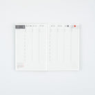 An open weekly planner with two grid pages, featuring a minimalist white design with light gray lines and small red date highlights, photographed on a clean white background.