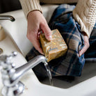 Person using SallyeAnder Hogwash stain removing soap on flannel clothing under water in sink