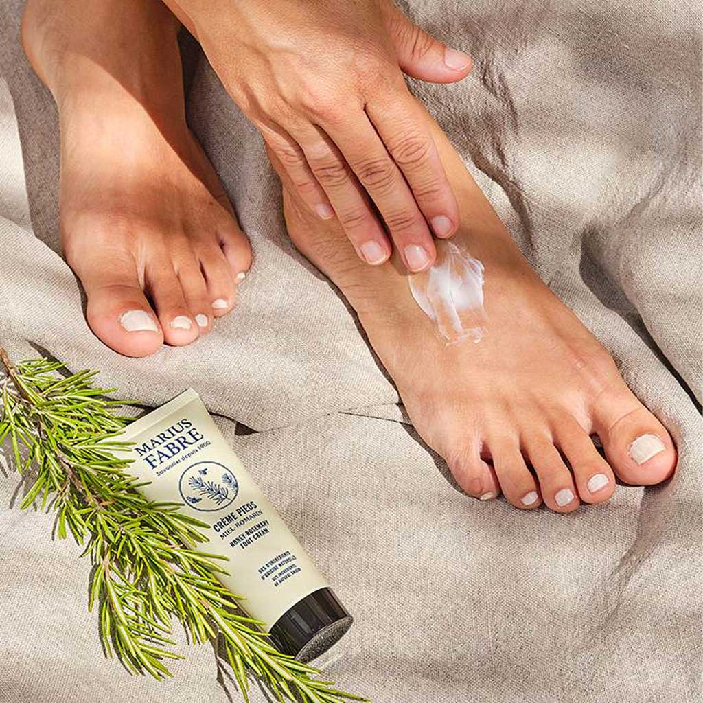 Person applying Marius Fabre honey and rosemary foot cream lotion on linen background