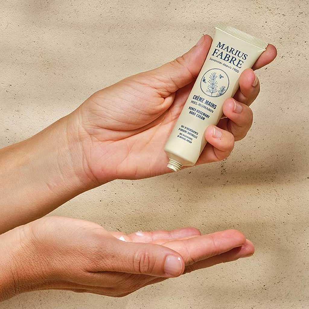 Hand applying a tube of Marius Fabre hand cream against a beige background