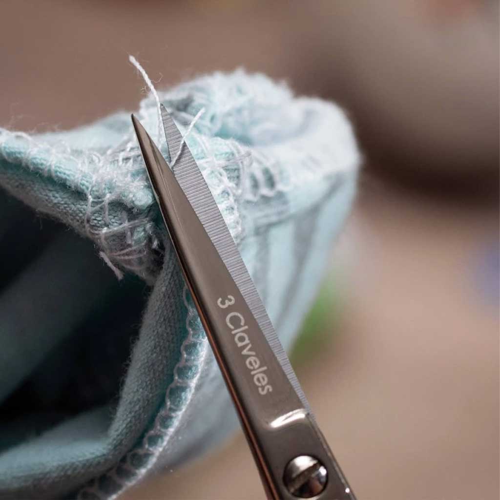 Scissors with '3 Claveles' branding cutting fabric