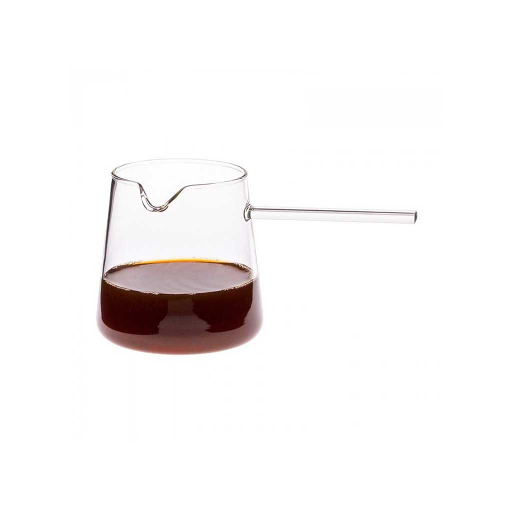 Clear glass coffee pitcher with a handle filled with dark liquid on a white background