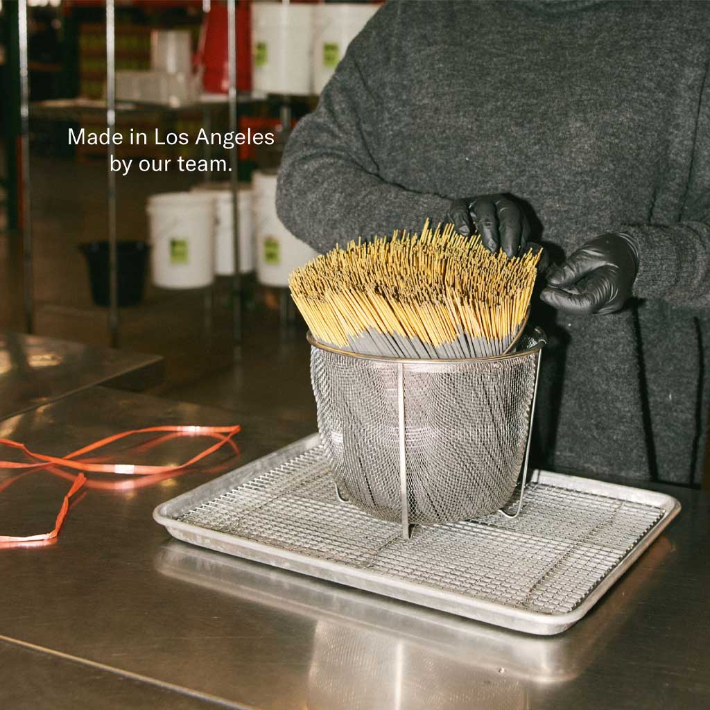 Person holding a basket of incense sticks on a metal tray in a kitchen setting with text 'Made in Los Angeles by our team.'