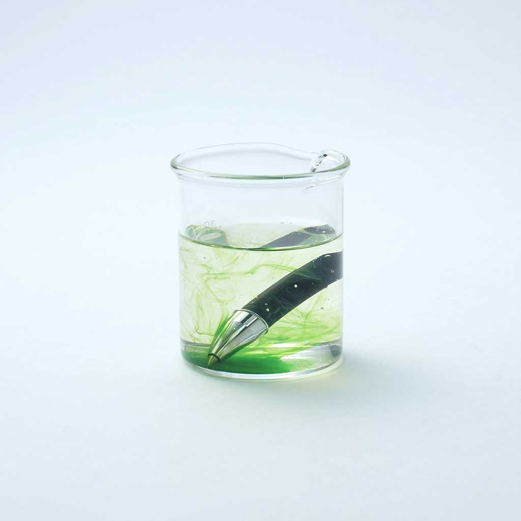 Rollerball pen nib being soaked in ink cleaning solution on light background