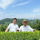 Two men standing in a tea field with a scenic background