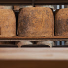 Close-up of three wheels of cheese on wooden shelf.
