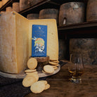 Box of cheese biscuits next to wheels of cheese, loose biscuits, and glass of liquid.