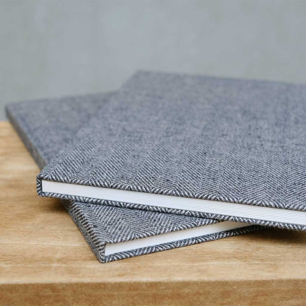 Two gray textured notebooks stacked on a wooden surface with a neutral background