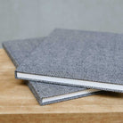 Two gray textured notebooks stacked on a wooden surface with a neutral background