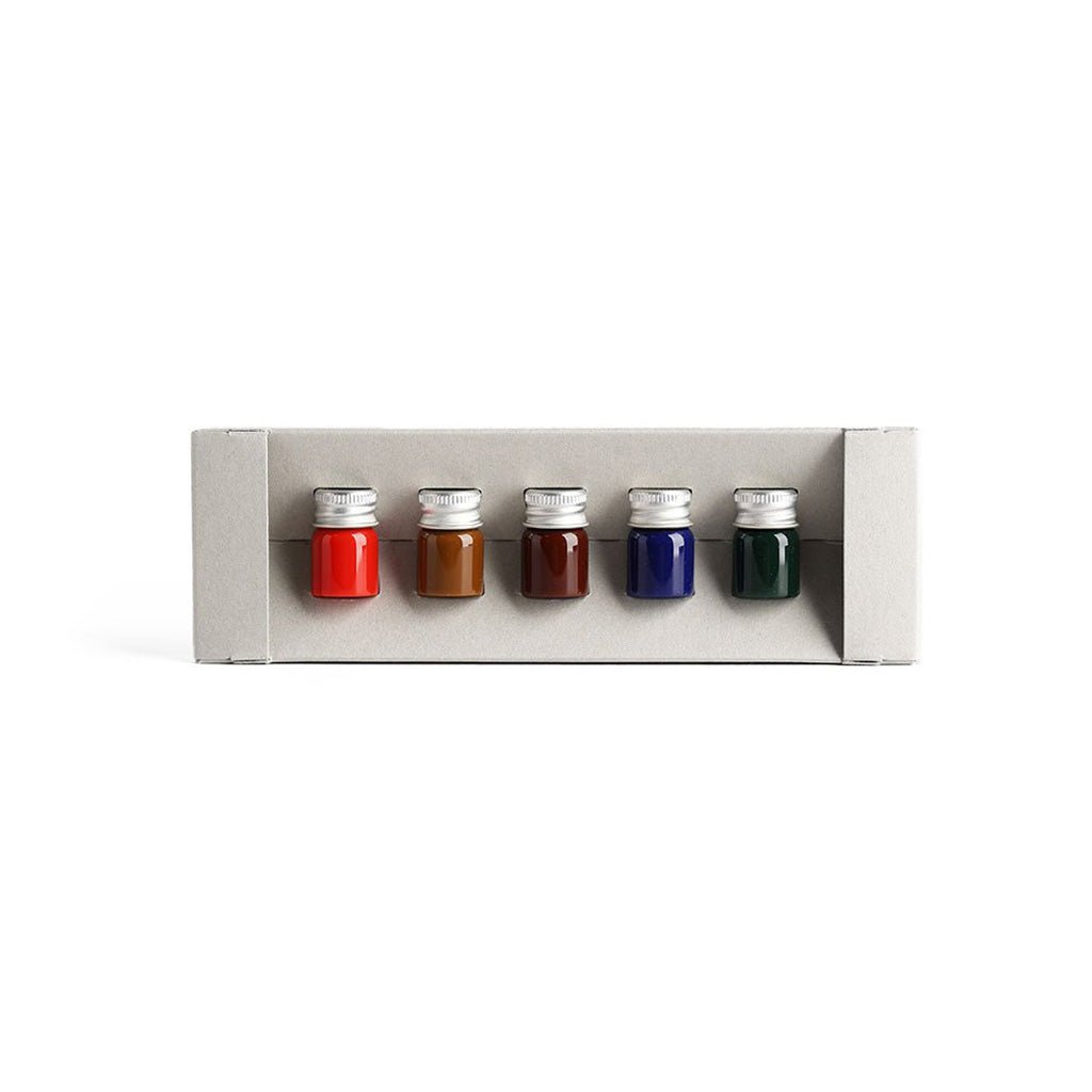 Set of five small bottles with colorful liquids in a gray holder on a white background