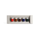 Set of five small bottles with colorful liquids in a gray holder on a white background