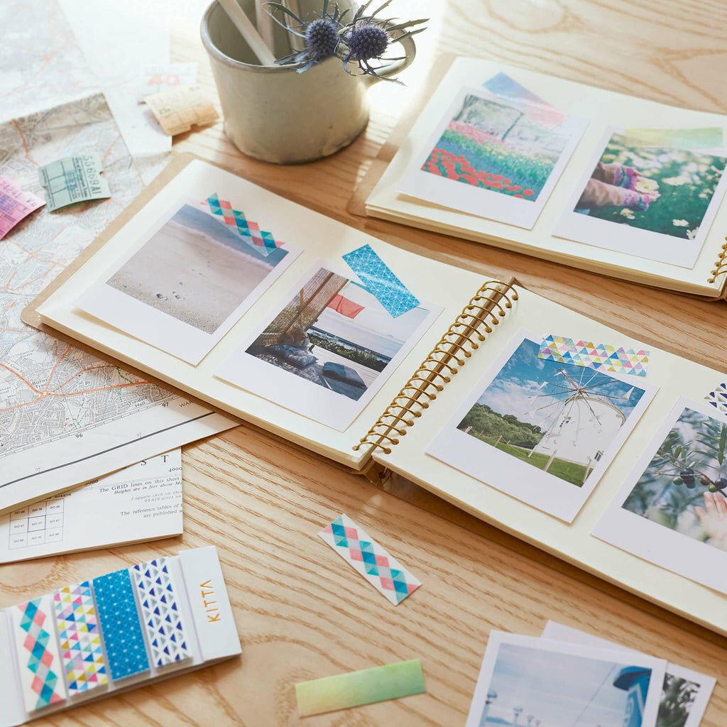 Open photo album with scenic photos taped with washi tape on a wooden surface with decorative items.
