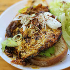 Sandwich with fried egg, avocado, and onions on a white plate
