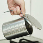 Metal measuring cup with handle and measurement markings, held by a hand.