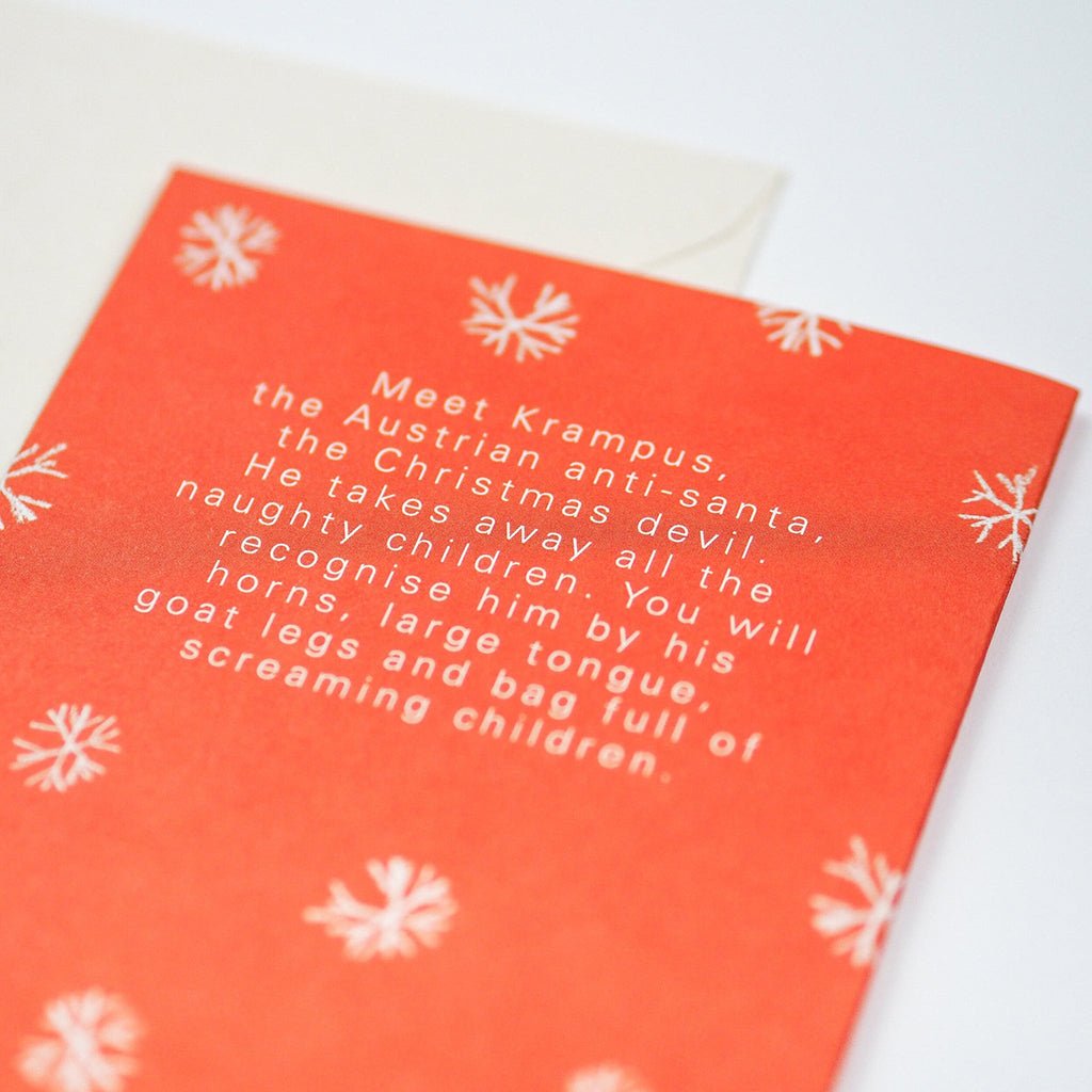 Red card with white text of Krampus myth and snowflake patterns on a white background