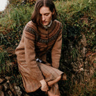 Woman in a patterned sweater sitting on a stone wall in a natural setting.