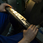 Close-up of hands holding knife blade with oil next to grinding belt in workshop