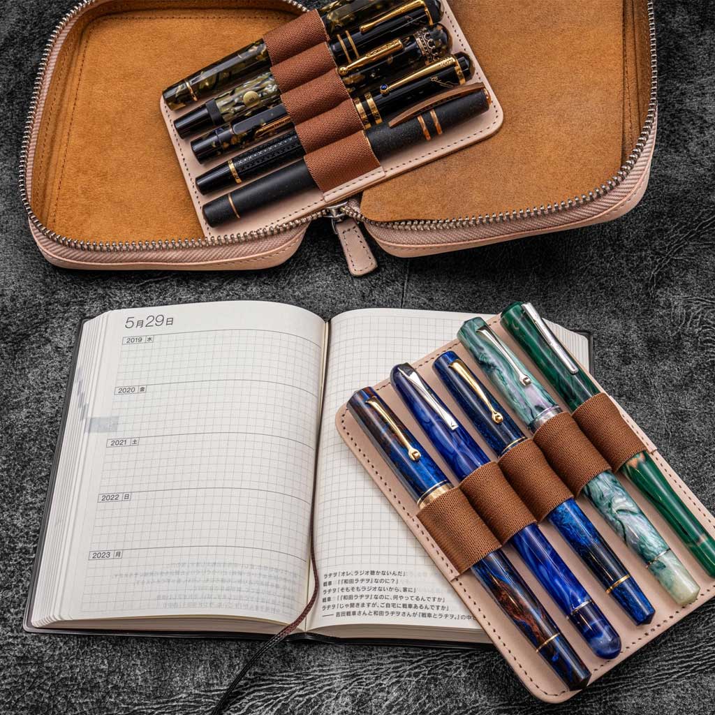 Natural undyed leather zippered pen pouch with removable holders and planner on a dark surface