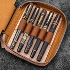 Natural undyed leather zippered pen pouch with five pens on a dark surface