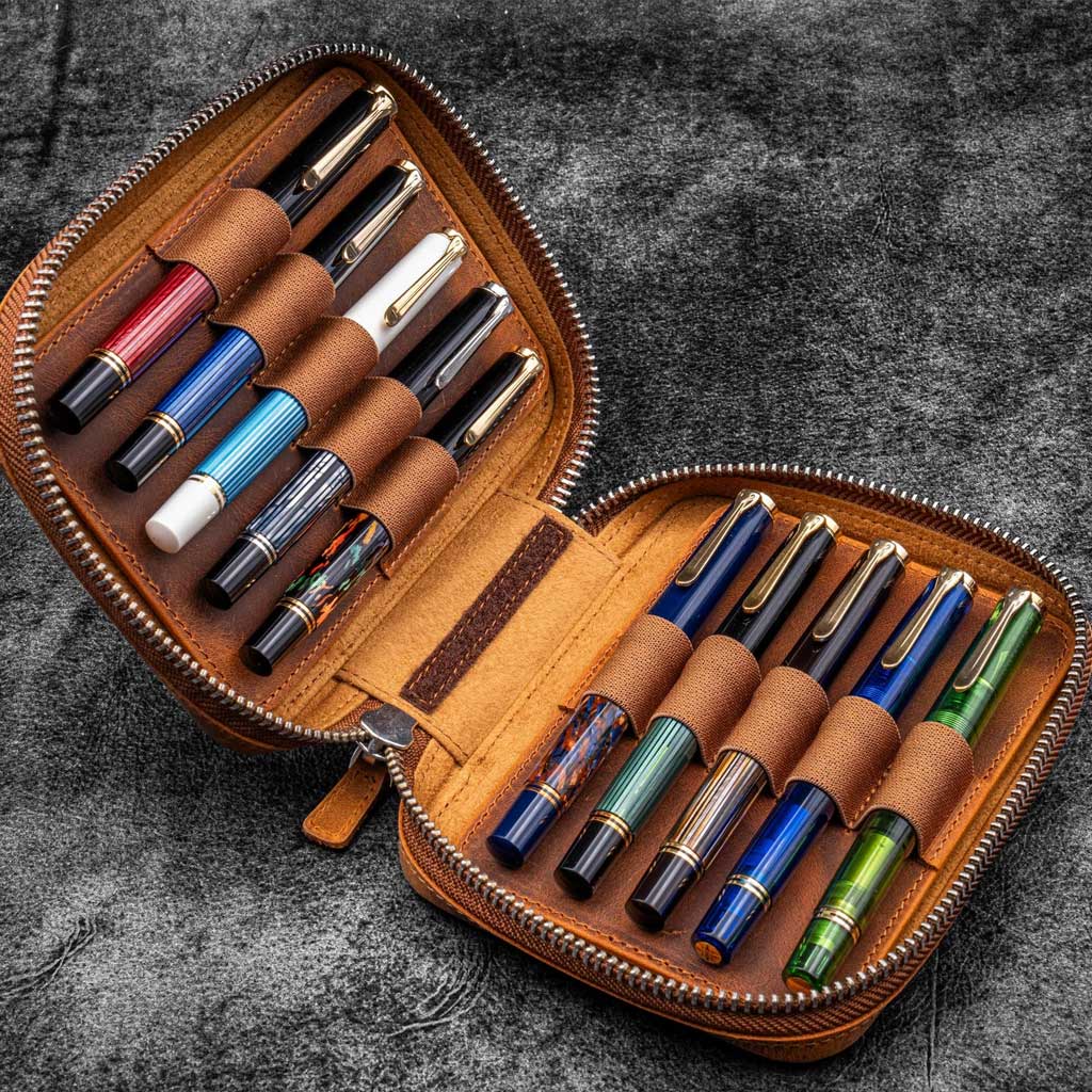 Brown leather zippered pen pouch with ten pens on a dark surface