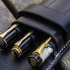 Three pens in Black leather pen case on wooden background
