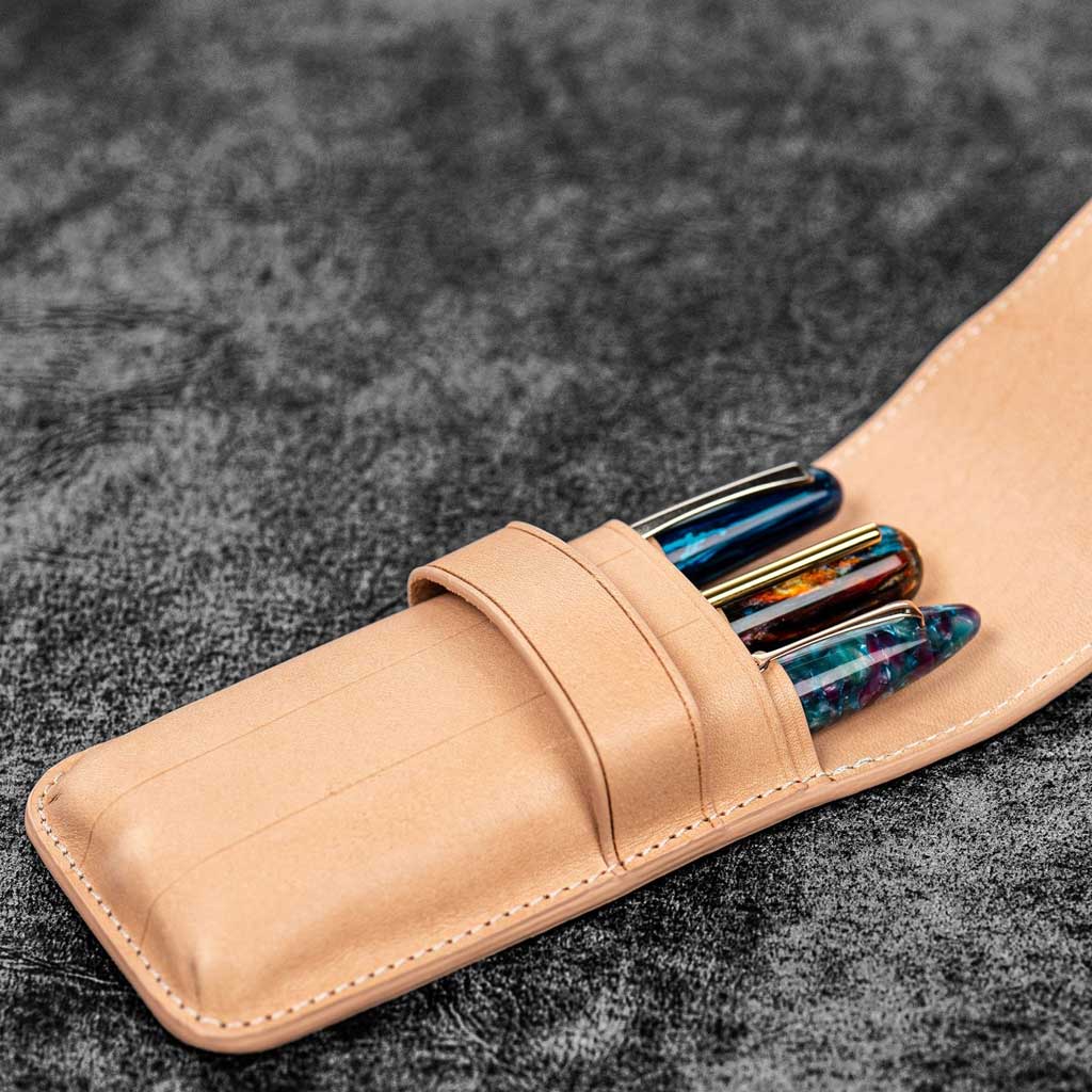 Three pens in undyed natural leather pen case on wooden surface
