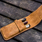 Three pens in brown leather pen case on wooden surface