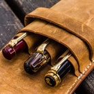 Three pens in brown leather pen case on wooden surface