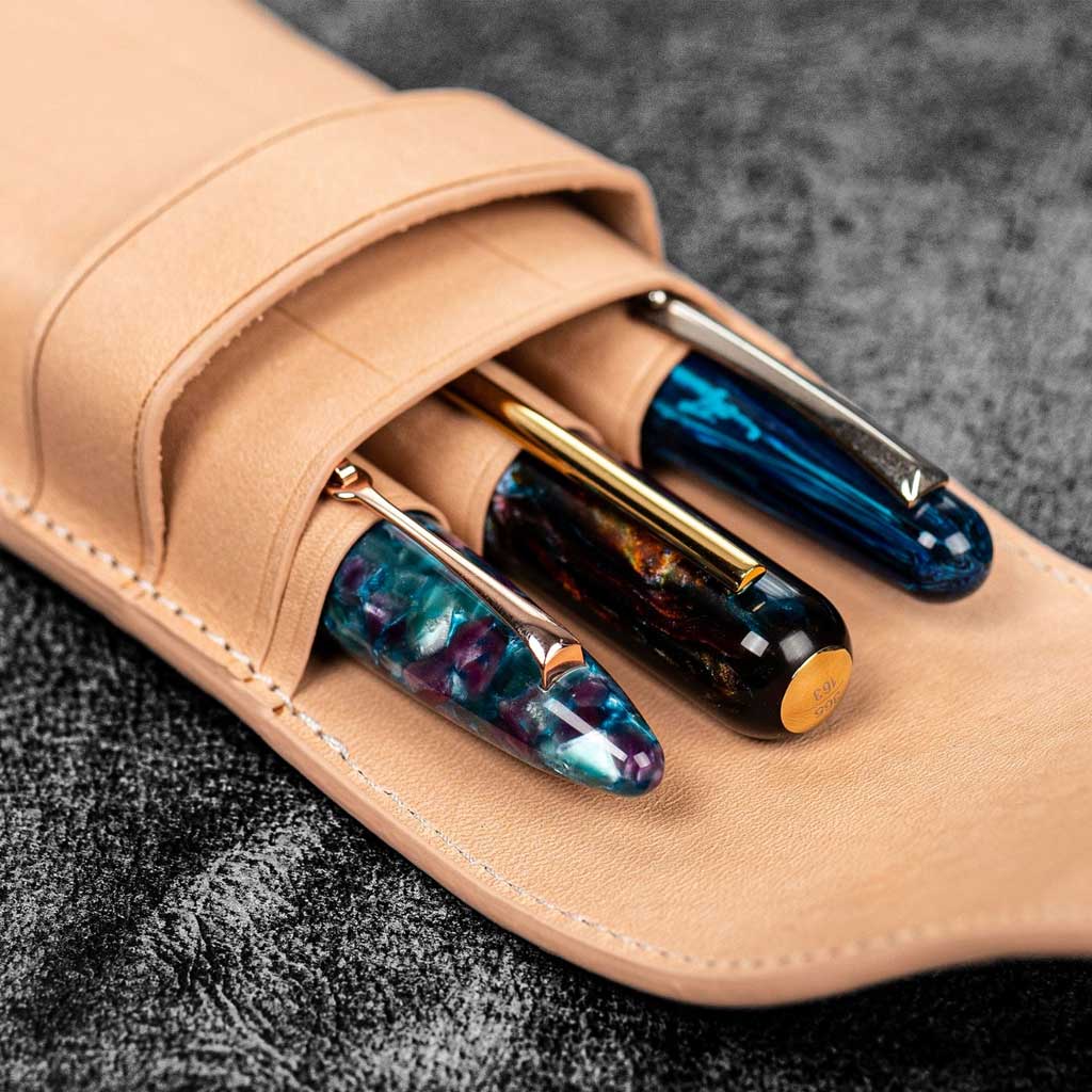 Three pens in undyed natural leather pen case on wooden surface