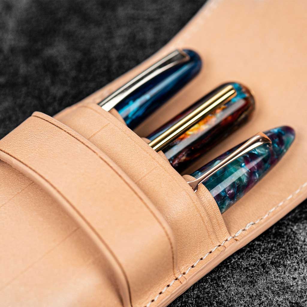 Three pens in undyed natural leather pen case on wooden surface