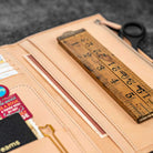 Open leather wallet insert with ruler, scissors, and other items on a textured surface