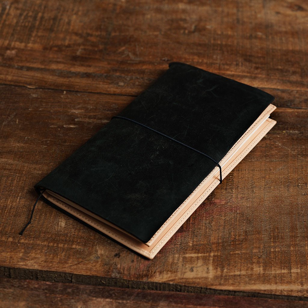 Black leather traveler's notebook with undyed natural leather wallet insert on wooden surface