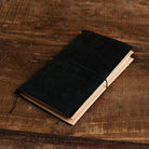 Black leather traveler's notebook with undyed natural leather wallet insert on wooden surface