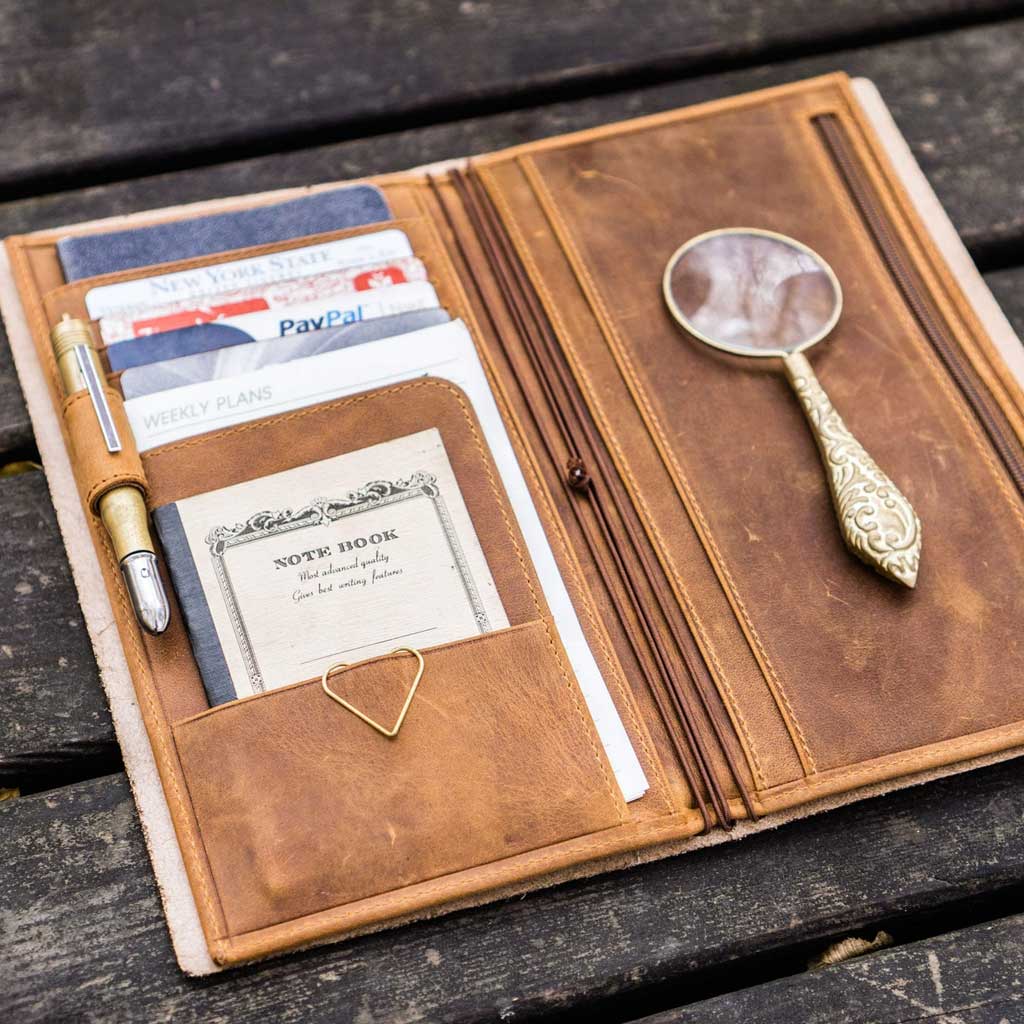 Brown leather Traveler's Notebook wallet insert with clips and papers on wooden surface