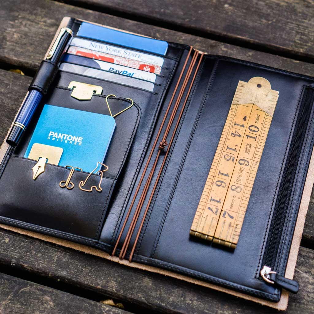 Black leather Traveler's Notebook wallet insert with clips and papers on wooden surface
