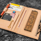 Natural undyed leather Traveler's Notebook wallet insert with clips and papers on textured surface