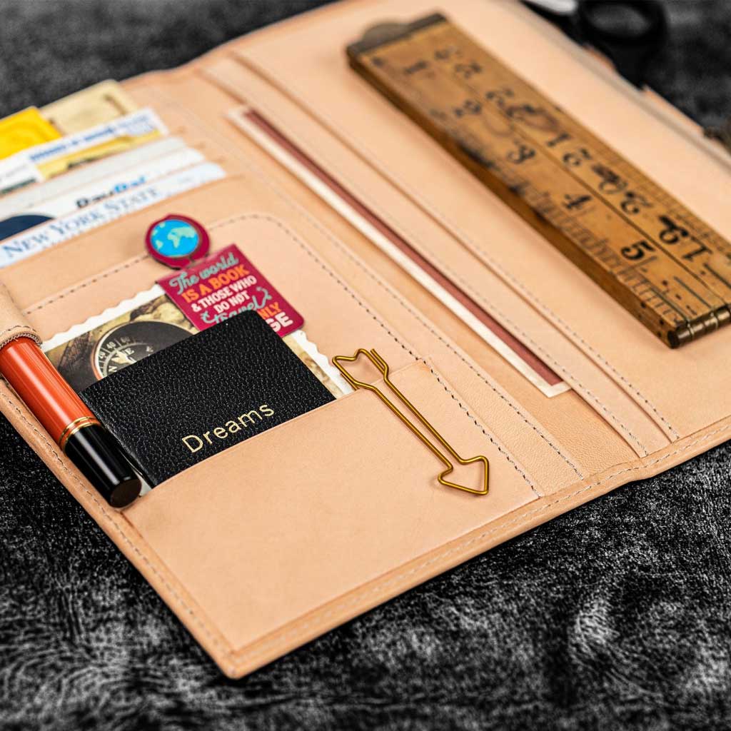 Natural undyed leather Traveler's Notebook wallet insert with clips and papers on textured surface