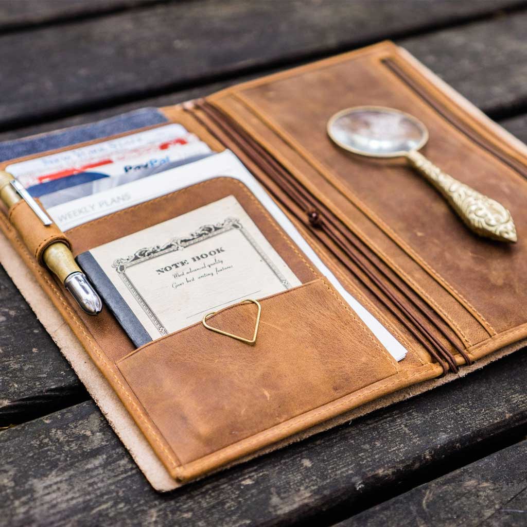 Brown leather Traveler's Notebook wallet insert with clips and papers on wooden surface