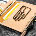 Close-up of a beige leather wallet with metal clip on a dark surface