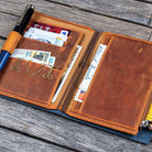 Brown leather wallet with various items on a wooden surface
