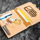 Open beige leather wallet with various cards and paper clips on a dark textured background