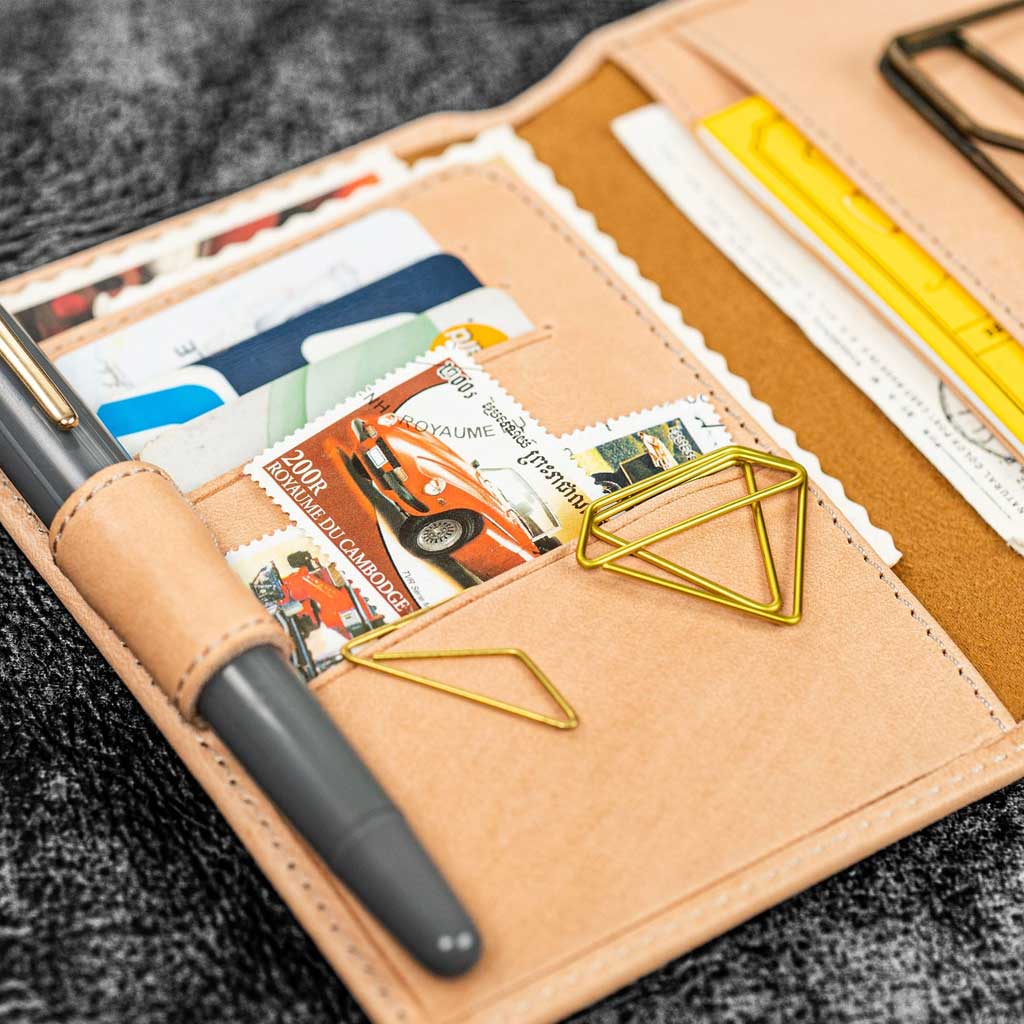 Undyed natural leather wallet insert with pen, clips, and papers on dark surface
