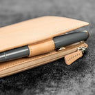 Close-up of a beige leather wallet with a pen and zipper detail on a dark textured background