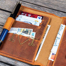 Brown leather wallet with money, cards, and a pen on a wooden surface