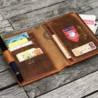 Brown leather wallet with various cards and a pen on a wooden surface