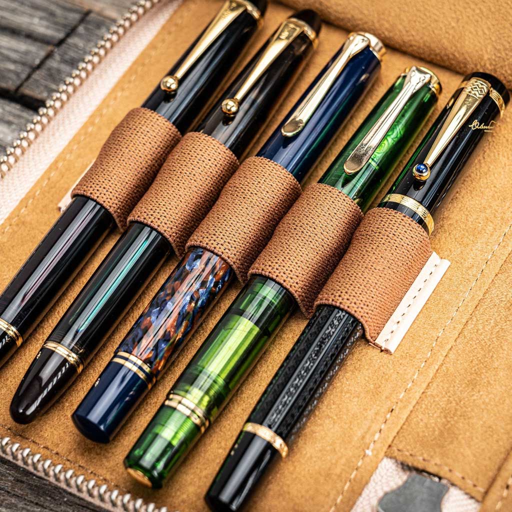 Natural undyed leather pen case with zipper and five pens on a wooden surface