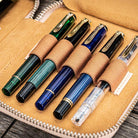 Natural undyed leather pen case with zipper and five pens on a wooden surface